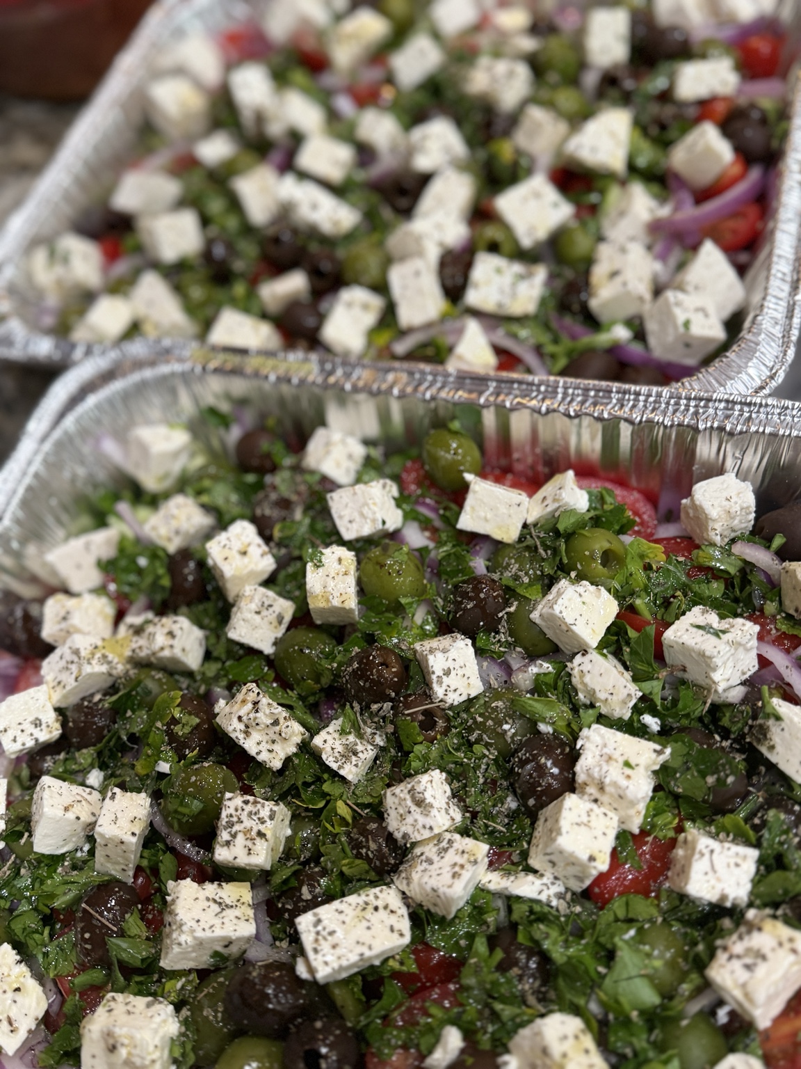Two catering trays of fresh salads topped with feta